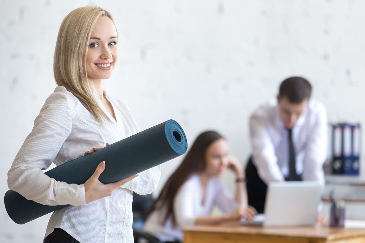 FirmenFitness Rundum-Sorglos-Mitgliedschaft Paket - Büro-Mitarbeiterin hat Yoga Matte unter dem Arm